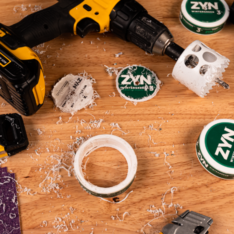 Wintergreen ZYN cans with a drill that was used to remove logo from lid on a wooden table.