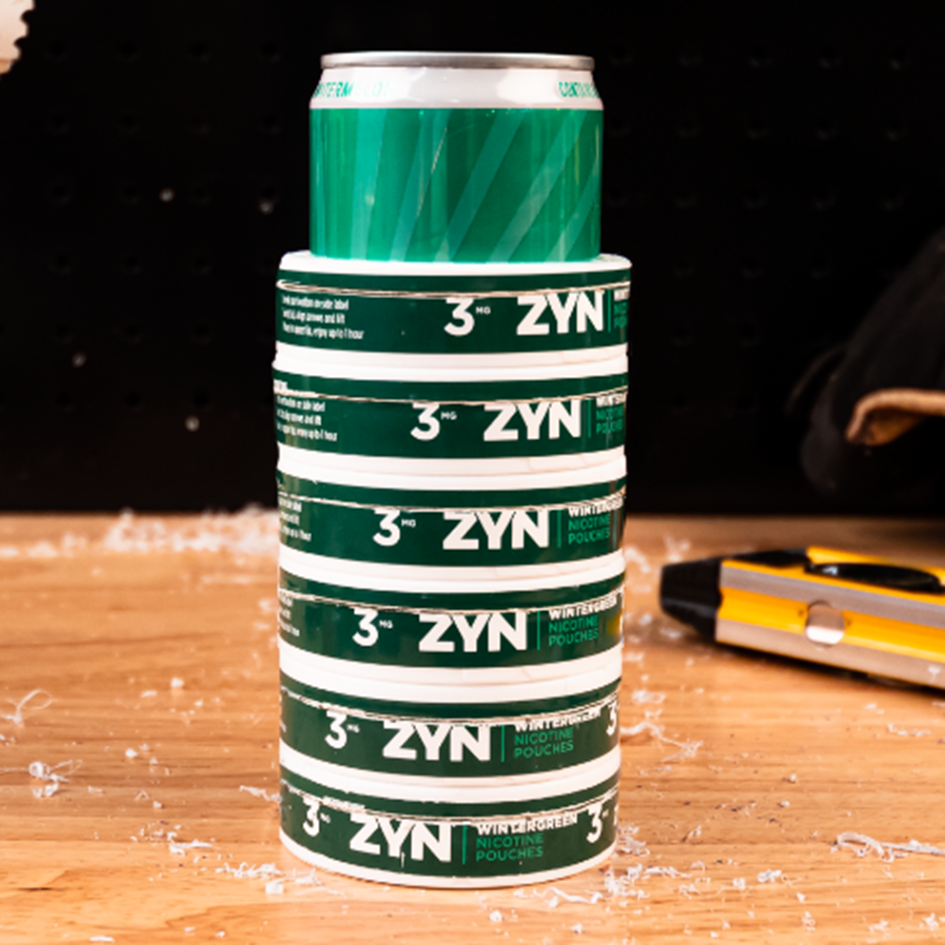 Six ZYN wintergreen cans stacked with a soda can inside.