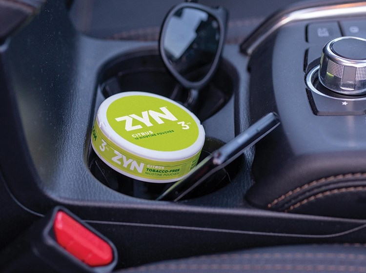 A can of Citrus ZYN Tobacco-Free Nicotine Pouches in a car cup holder.