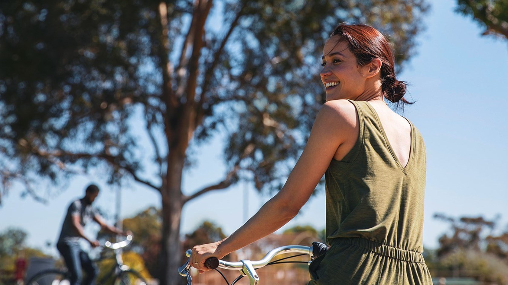 An adult woman in the sun holding her bike.