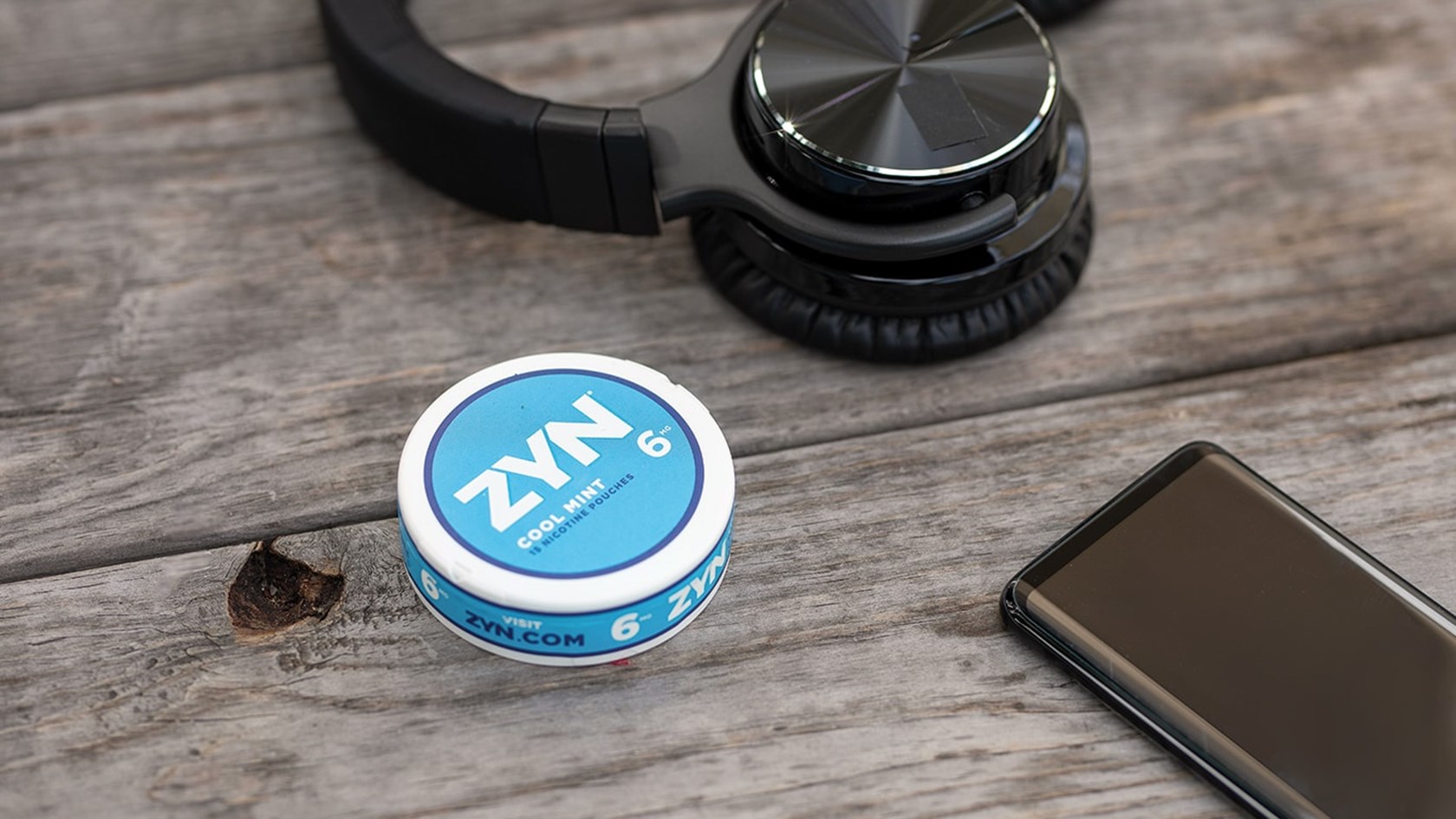 A can of Cool Mint ZYN Tobacco-Free Nicotine Pouches on a table next to a cell phone and headphones.