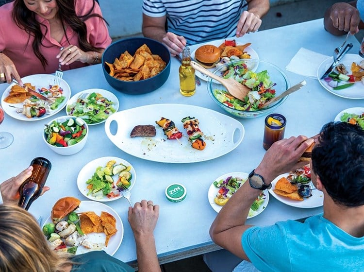 A group of adult friends eating a meal with cans of ZYN Tobacco-Free Nicotine Pouches on the table.